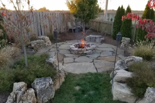CanAm Professional Landscaping - landscaping project with flagstone patio in fenced backyard, with stone seating around stone fire put, surrounded by plant and flower beds - Girard, IL