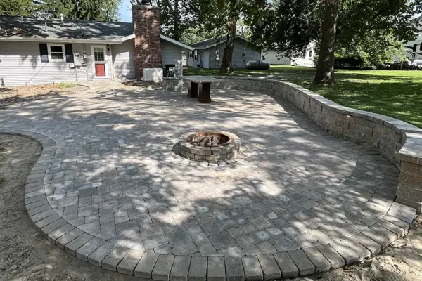 CanAm Professional Landscaping - landscaping project with large backyard patio of stone, stone wall/bench, permanent table and fire pit - Girard, IL